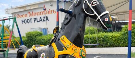 A black and yellow carousel horse at a playground with a sign reading "Green Mountain Foot Plaza" in the background.