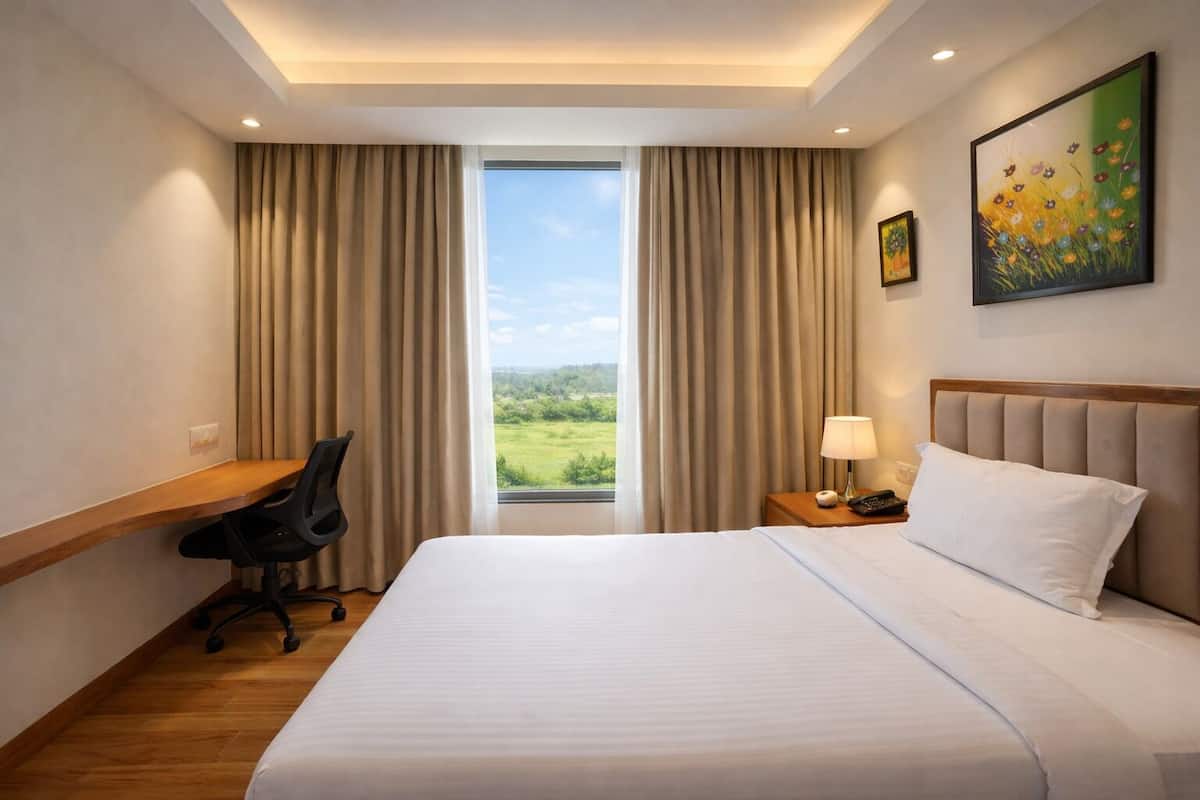 Una habitación de hotel con cama, escritorio, silla, mesita de noche con lámpara y un cuadro.
