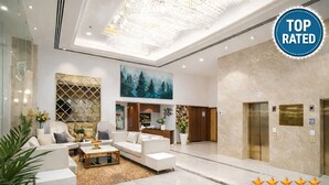 A modern lobby with a chandelier, white sofas, a coffee table, and a painting of a forest. - GREEN MOUNTAIN RESORT - Guna (Guna)