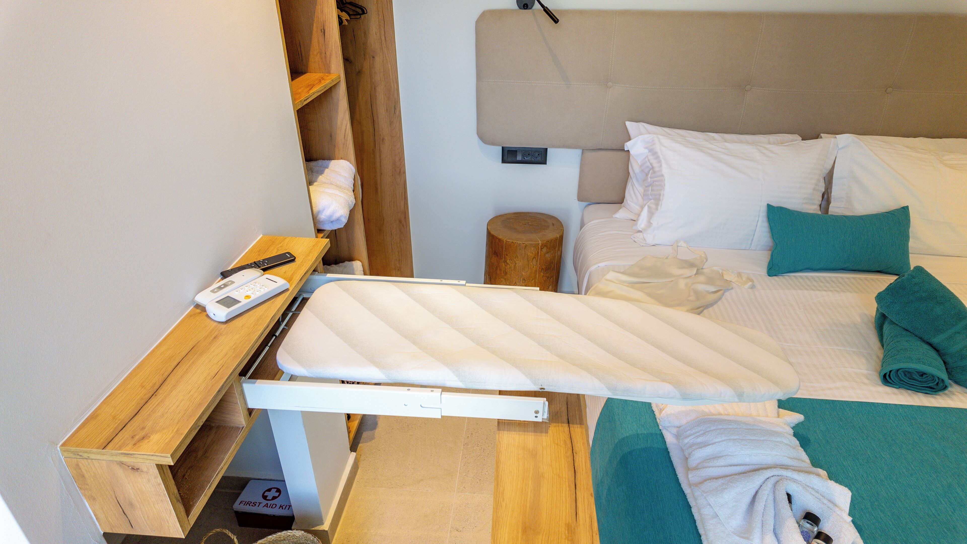 A neatly made bed with a white mattress, teal towels, and a first aid kit in a wooden drawer.