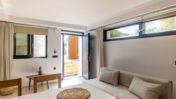 Una sala de estar moderna con un sofá, una mesita y una silla. Hay un ventanal corredero que da a un espacio exterior con un muro de piedra y listones de madera.