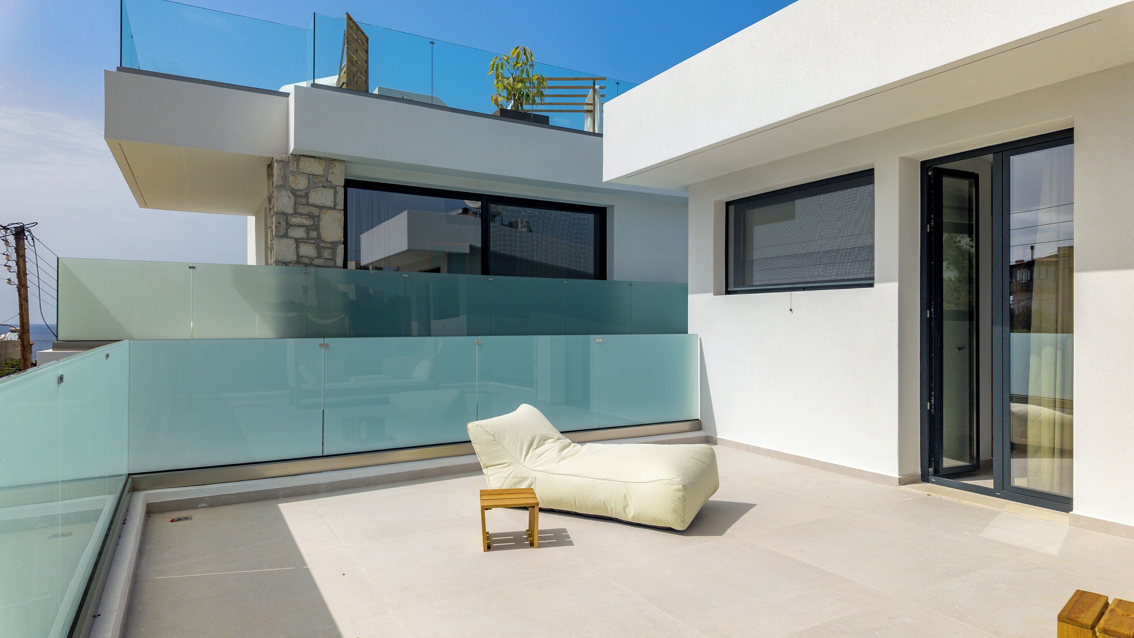 Un espacio exterior moderno con barandilla de cristal, un sofá blanco y una pequeña mesa de madera.