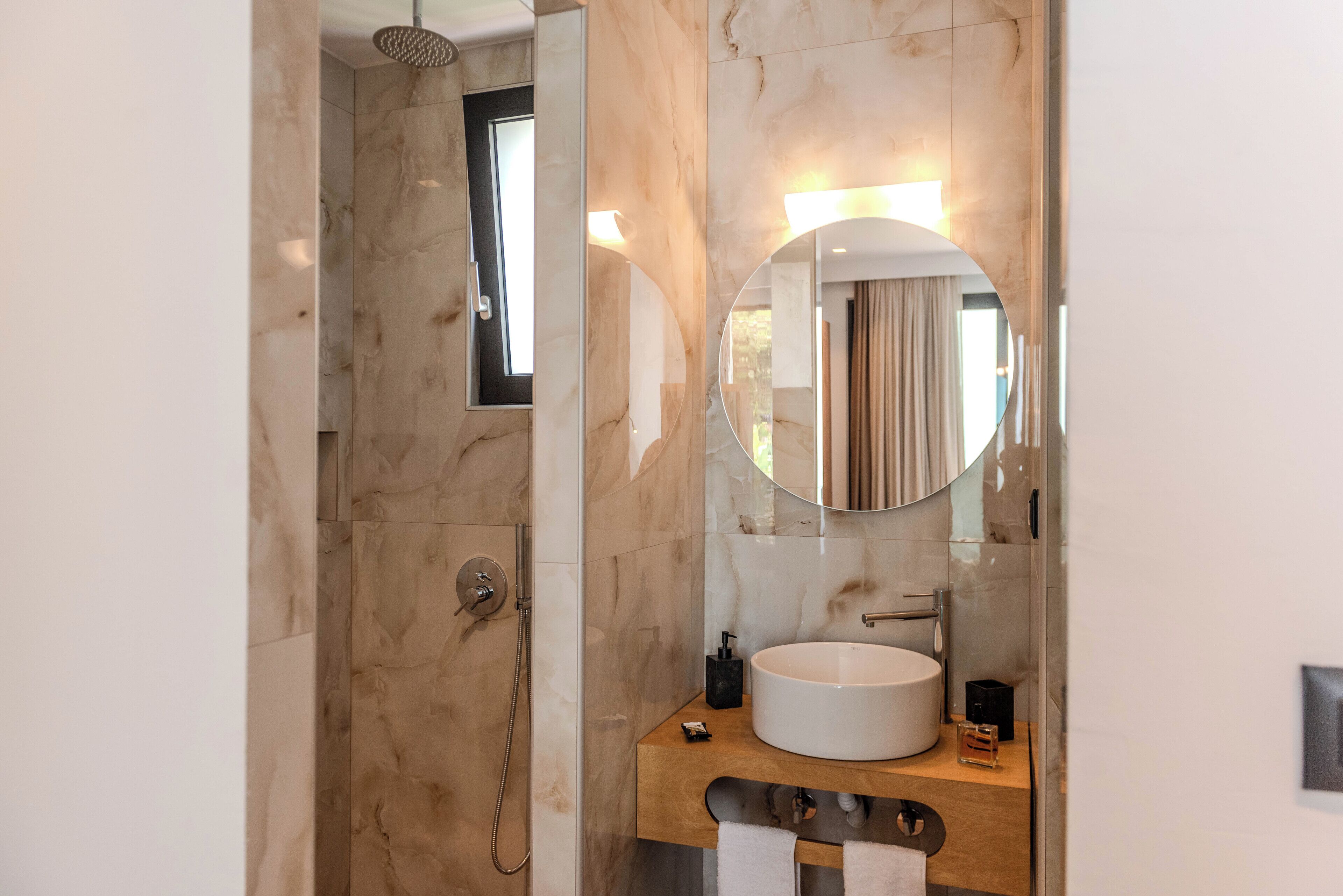 Un baño moderno con pared de mármol, un espejo redondo, un lavabo y una ducha.