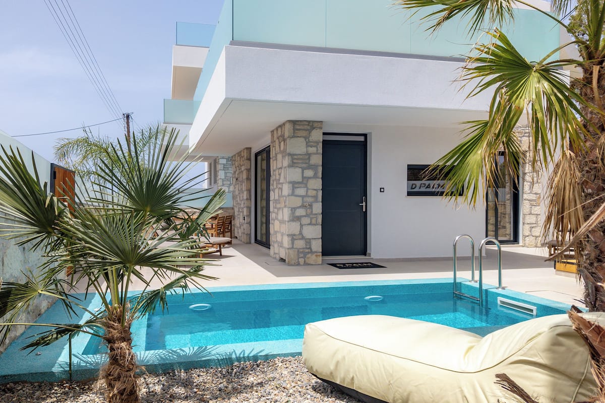 A modern pool area with a stone wall, palm trees, and a beige lounge chair.