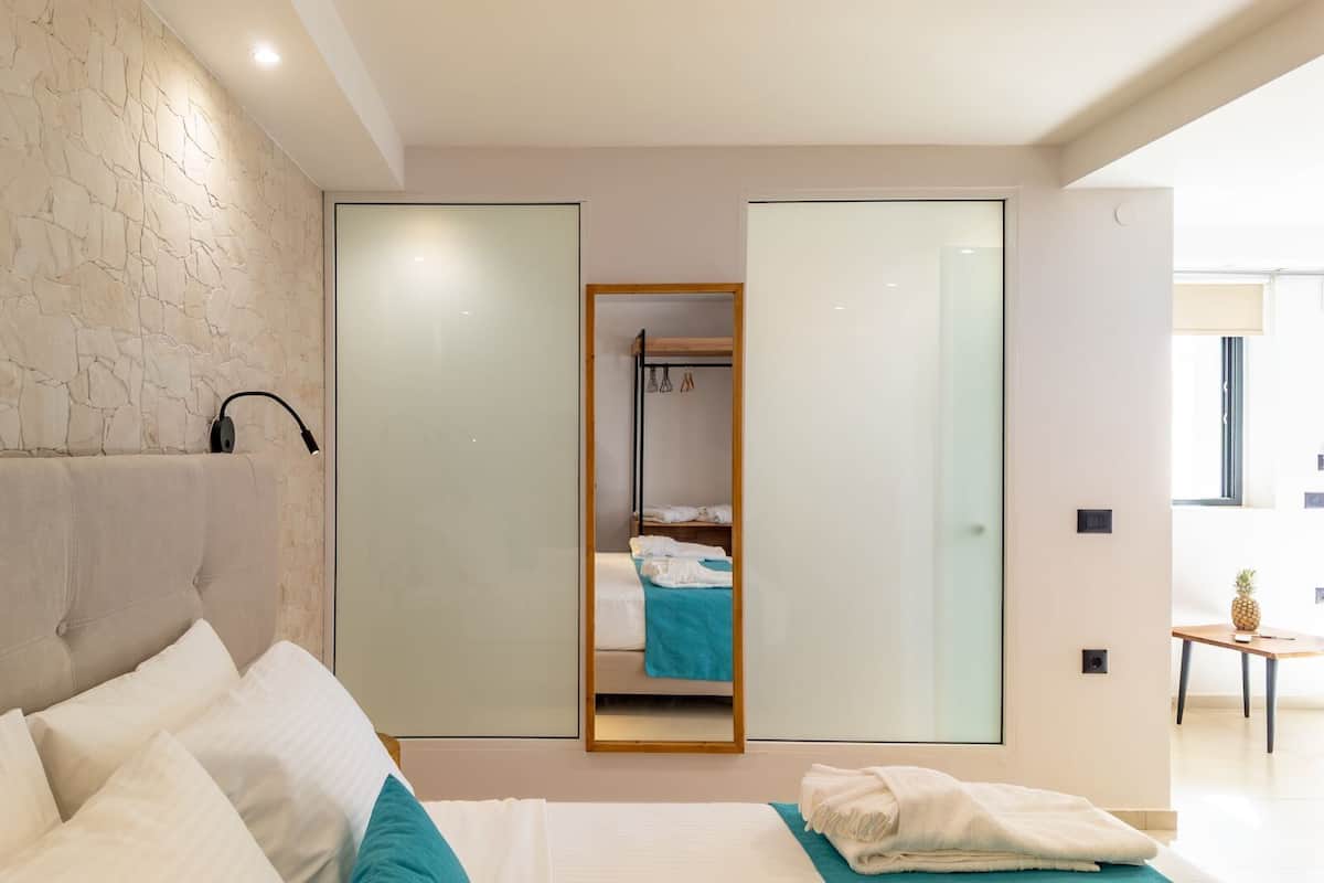 A modern bedroom with a large bed, a stone-textured wall, a mirror, and a view of a bathroom.