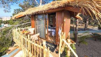 Una cabaña de madera con techo de paja, un balcón y una cama con sábanas blancas.