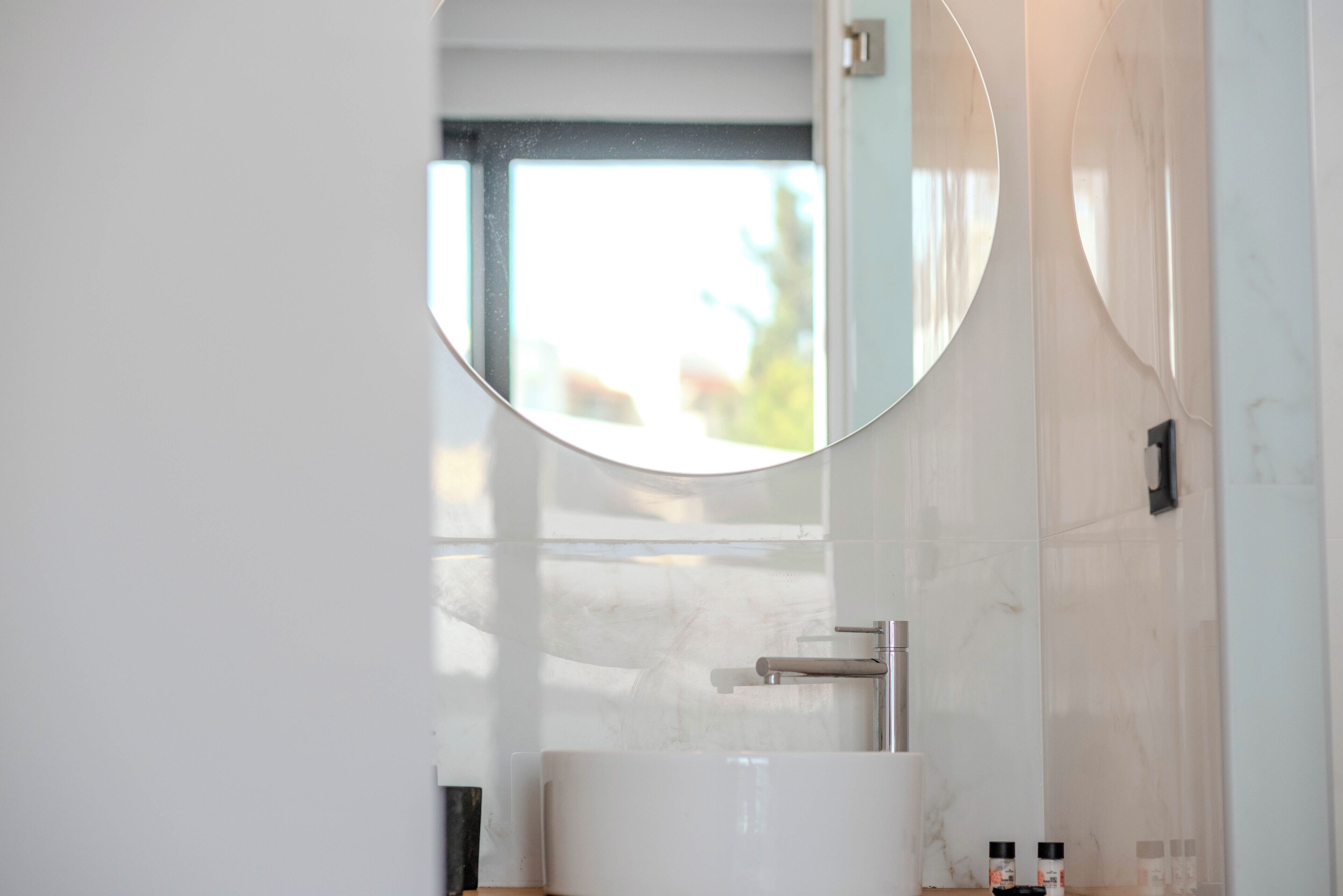 Een moderne badkamer met een grote spiegel, een witte wastafel en een raam dat voor natuurlijk licht zorgt.