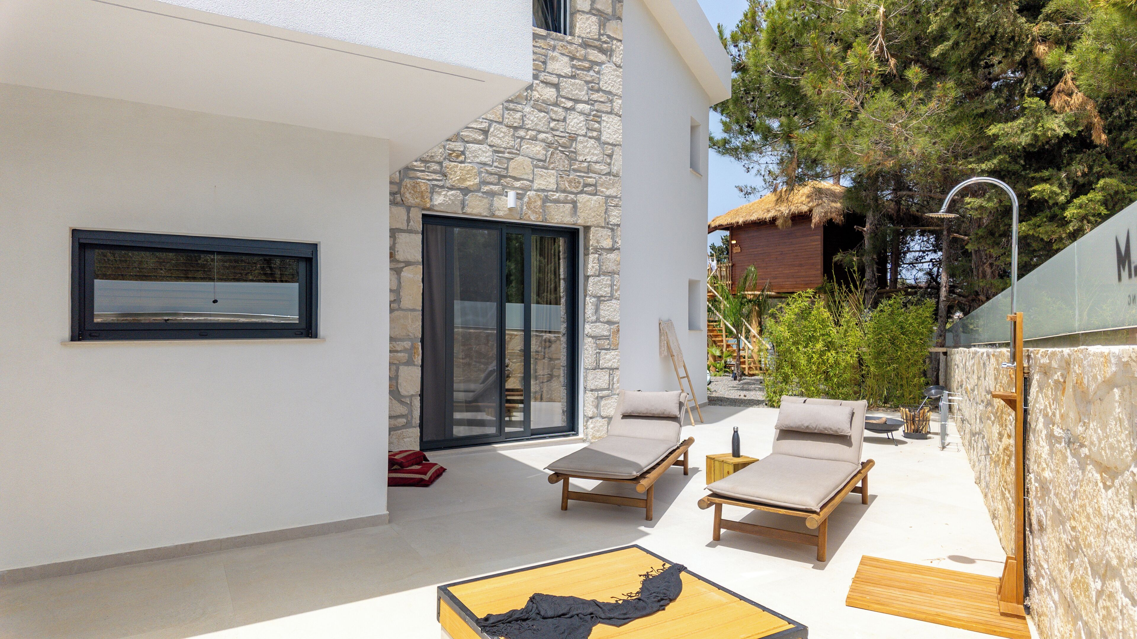 Un patio extérieur moderne avec deux fauteuils de jardin en bois, une petite table et un mur en pierre.