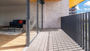 Un balcón moderno con suelo de madera, puerta de vidrio y barandilla negra.
