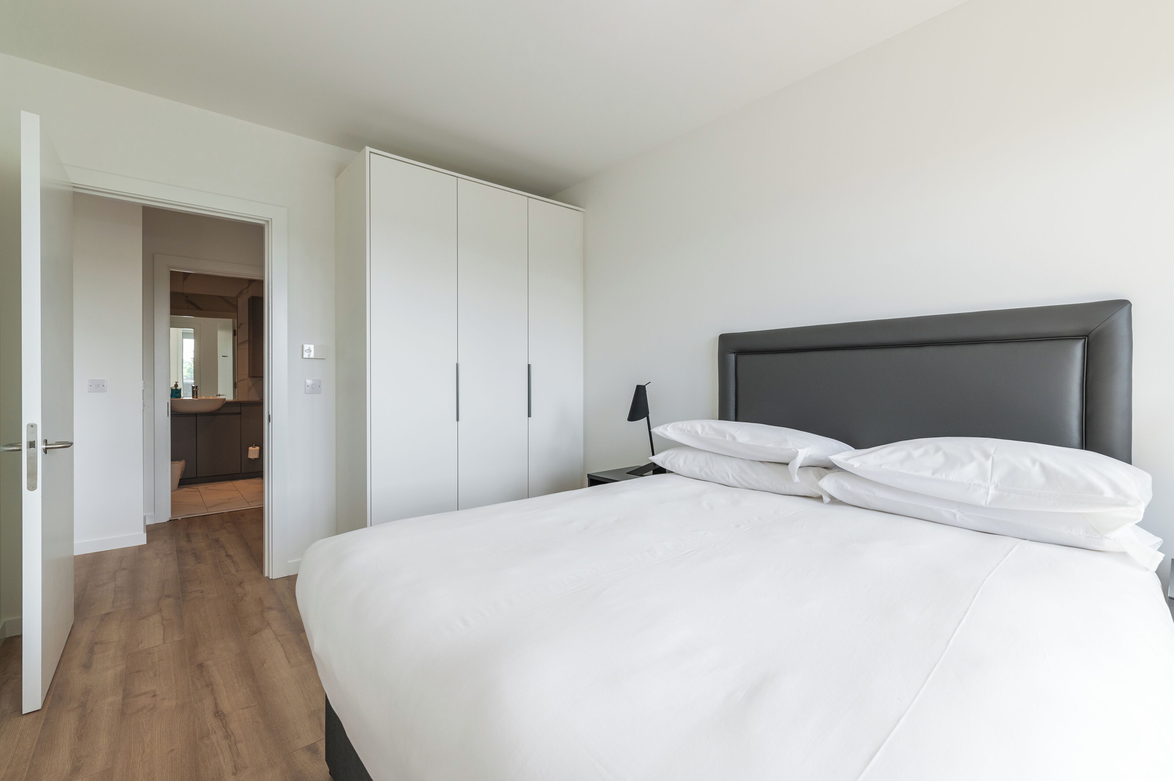 A bedroom with a large bed, white bedding, a dark headboard, and a wardrobe.