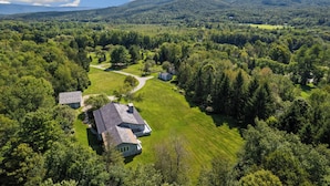 An aerial view of a property with multiple buildings, a well-maintained lawn, and a forested area with a mountain in the background. - Private 5-BR Mountain Estate 10-Min to Manchester (Dorset)