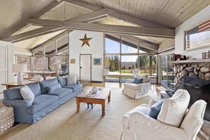 Un vaste salon doté d’un haut plafond, d’une cheminée en pierre et de grandes fenêtres offrant une vue sur l’extérieur.