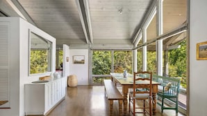 A spacious room with a wooden dining table, benches, and a view of greenery through large windows. - Private 5-BR Mountain Estate 10-Min to Manchester (Dorset)