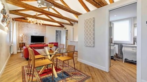 A modern living room with exposed wooden beams, a brick wall, a glass dining table, and a red sofa. - Charming and Elegant Venetian Retreat with Rooftop Views
 (Venezia)