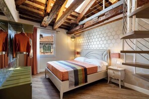 A bedroom with a wooden ceiling, a bed with a striped blanket, a nightstand, and a view of a building through a window. - Charming and Elegant Venetian Retreat with Rooftop Views
 (Venezia)