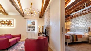 A modern living room with a red sofa, a red pouf, a wooden ceiling, and a view of a building through a window. - Charming and Elegant Venetian Retreat with Rooftop Views
 (Venezia)