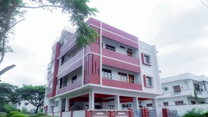 A multi-story building with a red and white facade, balconies, and a gated entrance. - Coorg Residency Homestay (Somvarpet)