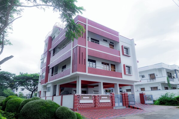 Un edificio de varios pisos con fachada roja y blanca, balcones y una entrada con reja.