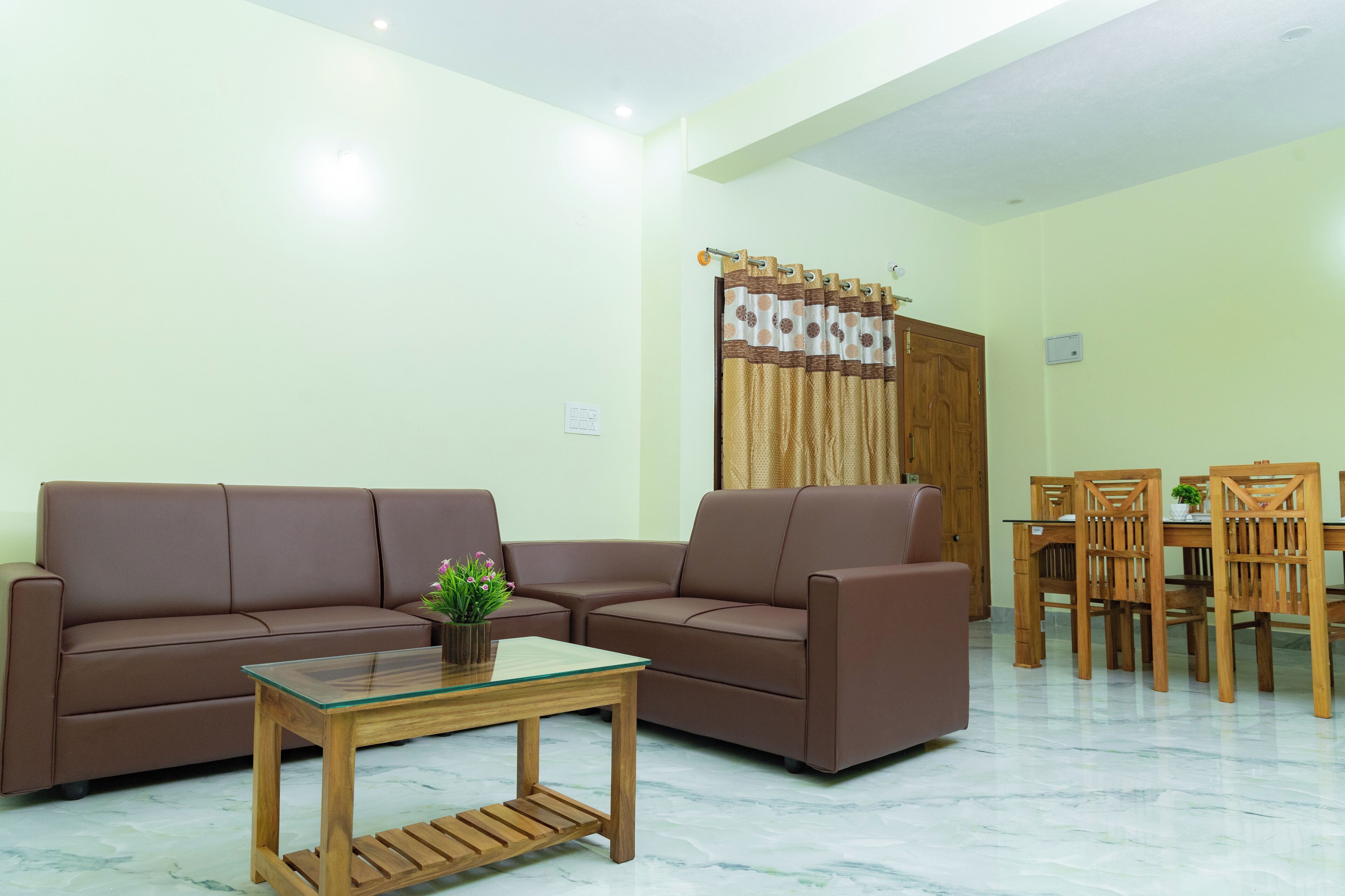 Una sala de estar con un sofá marrón, una mesa de centro de vidrio y una mesa de comedor con sillas de madera.