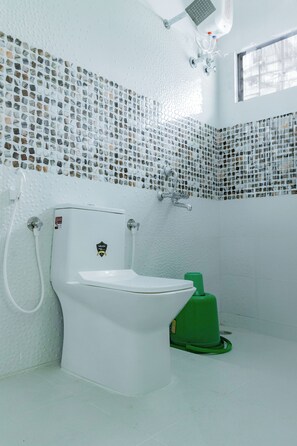 Un baño con inodoro blanco, un bidé verde y una pared de azulejos con diseño de mosaico.