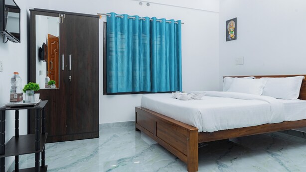 A bedroom with a wooden bed, a nightstand, a mirror, a wardrobe, and a window with curtains. - Coorg Residency Homestay (Somvarpet)