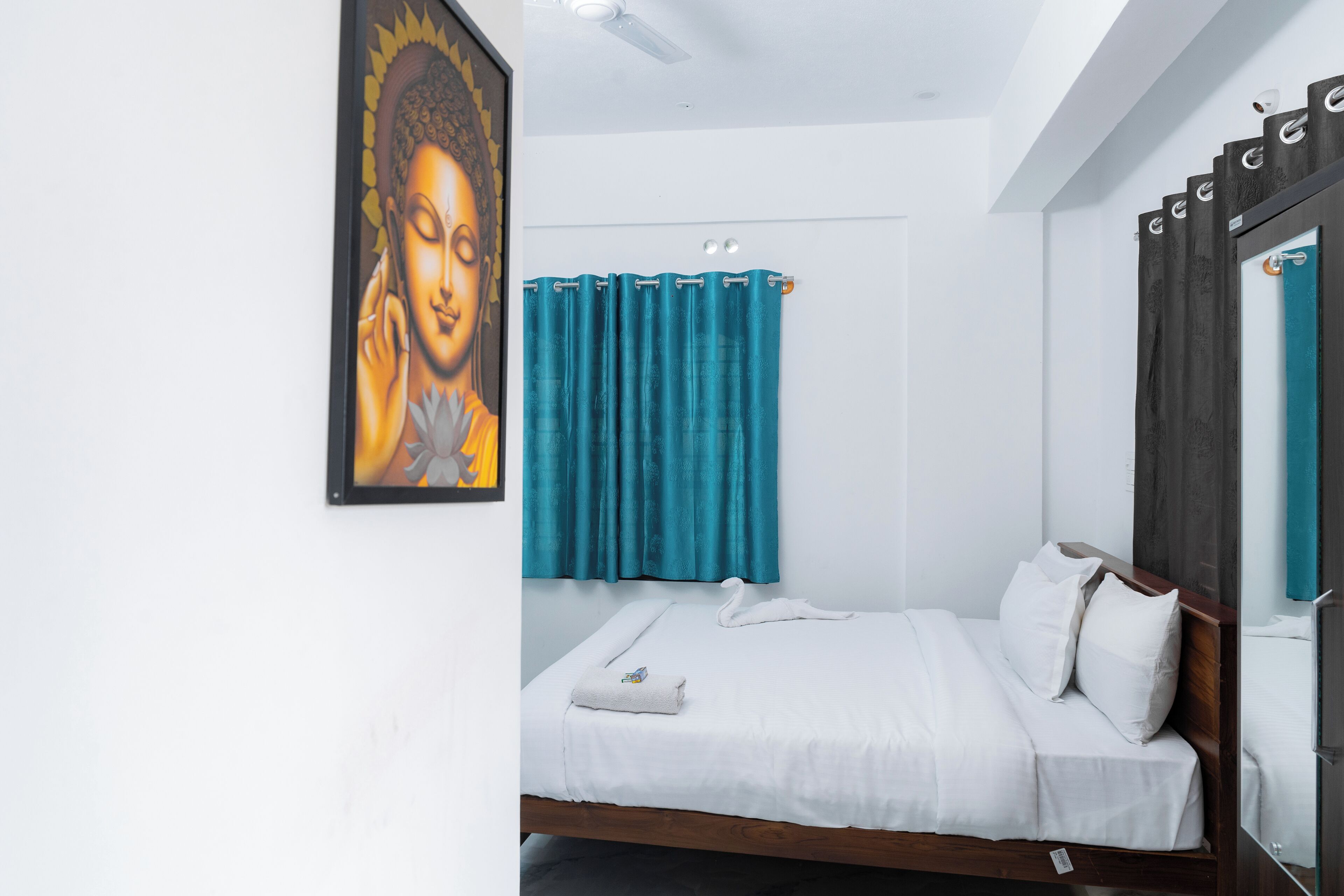 A bedroom with a bed, white bedding, a blue curtain, and a framed picture on the wall.