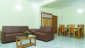 A living room with a brown sofa, a glass coffee table, and a wooden dining table with chairs. - Coorg Residency Homestay (Somvarpet)