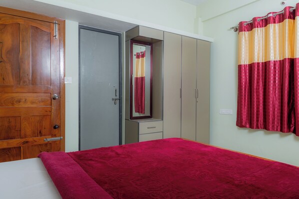 A bedroom with a wooden wardrobe, a mirror, a bed with a red blanket, and a curtain. - Coorg Residency Homestay (Somvarpet)
