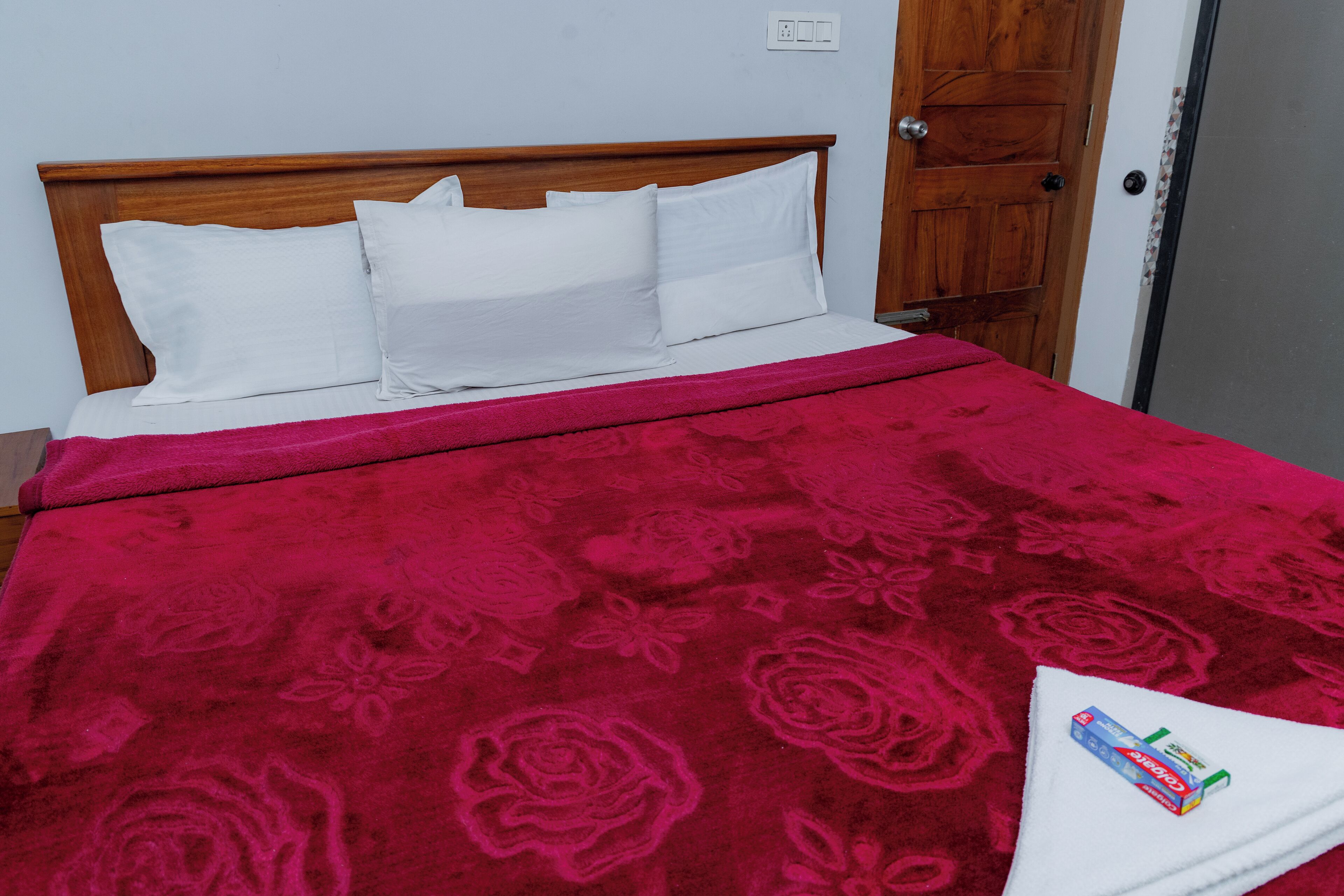 A bed with a wooden headboard, white pillows, and a red floral bedspread.