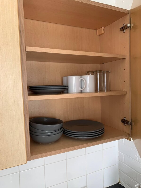 A kitchen with wooden shelves and cabinets, containing plates, bowls, and mugs. - Seaside Retreat Sleeps 4 With Pets (Brighton)