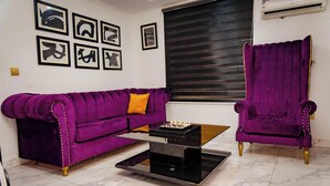 A living room with a purple sofa, a matching armchair, a coffee table, and a chessboard. - Luxury Hotel Deluxe Room - Sleeps 2 - Gym - Pool (Lekki)