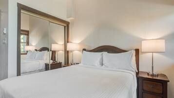 A neatly made bed with white linens, a large mirror, and two bedside lamps on wooden nightstands.