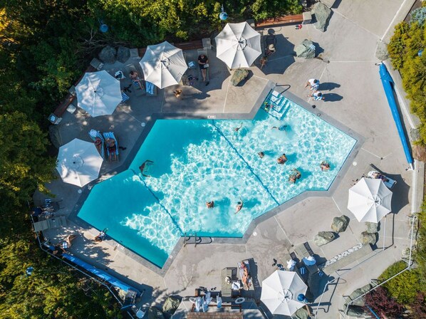 En vy från ovan av ett poolområde med flera solstolar, parasoller och en pool där folk badar.