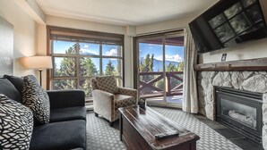 A living room with a sofa, armchair, coffee table, fireplace, and a TV mounted on the wall. - 1B Ski-In/Out Upper Floor Suite with Mountain View (Whistler)
