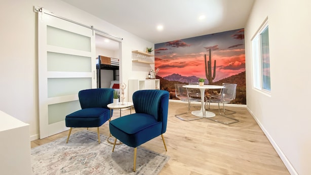Une pièce moderne avec deux fauteuils bleus, une petite table ronde et une fresque représentant un coucher de soleil dans le désert.