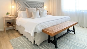 Une chambre bien rangée, avec un lit, des tables de chevet, un banc et une grande fenêtre avec des rideaux.