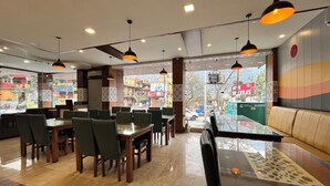 A restaurant interior with tables and chairs, a glass partition, and a view of the street outside. - HOTEL SHIV VILAS (Rishikesh)