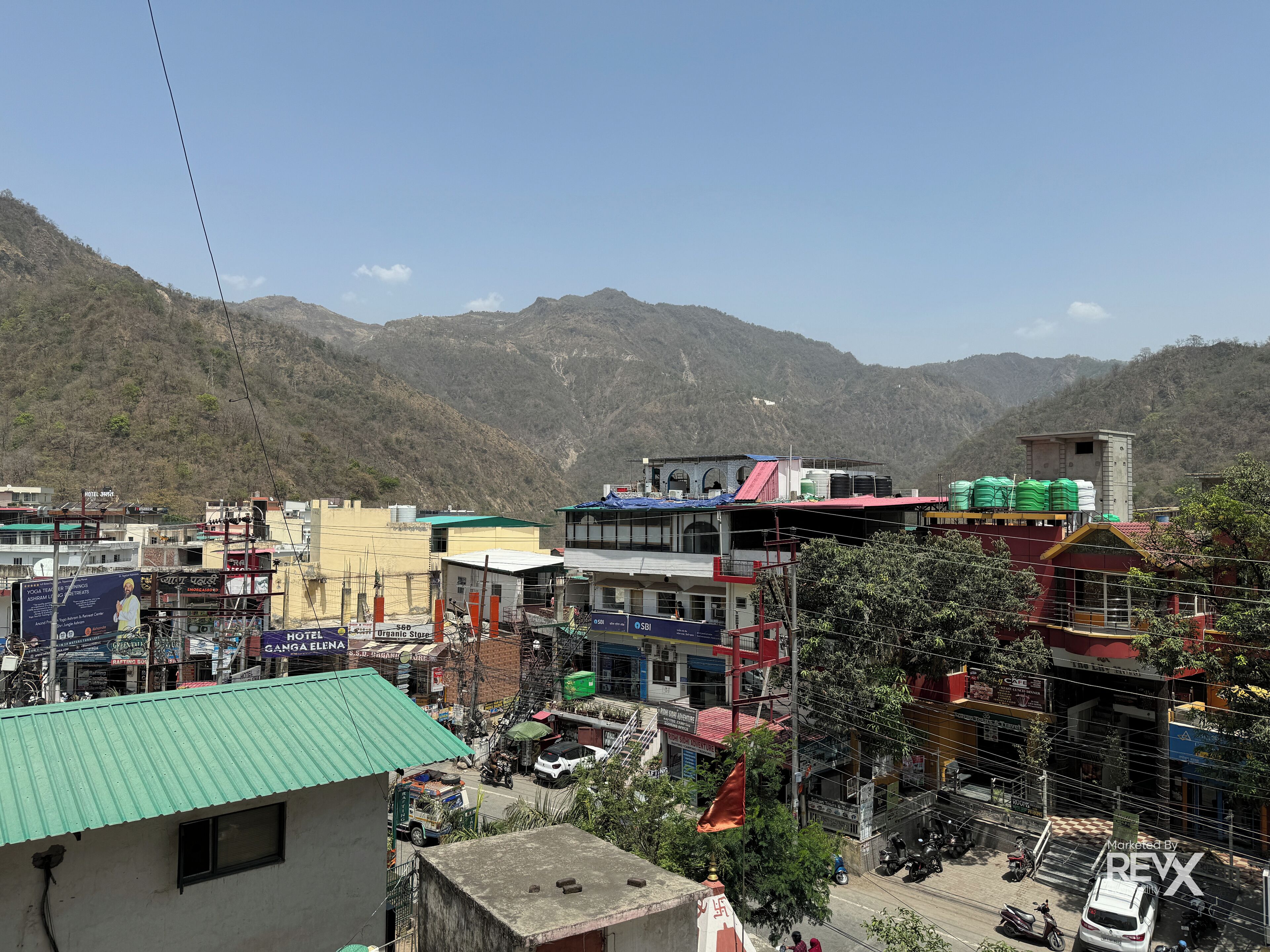 A multi-story building with a green roof, surrounded by other buildings and a mountainous backdrop.