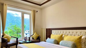 A hotel room with a large bed, a chair, a table, and a view of greenery outside. - HOTEL SHIV VILAS (Rishikesh)
