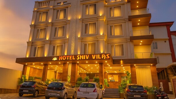 A multi-story hotel with a prominent entrance, a sign reading "HOTEL SHIV VILAS," and several parked cars in front. - HOTEL SHIV VILAS (Rishikesh)