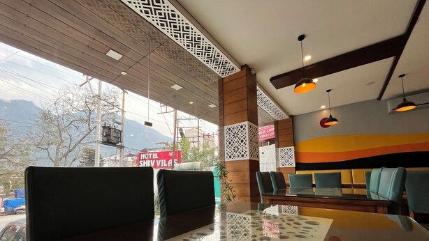A modern hotel lobby with a glass partition, seating area, and a view of the mountains. - HOTEL SHIV VILAS (Rishikesh)