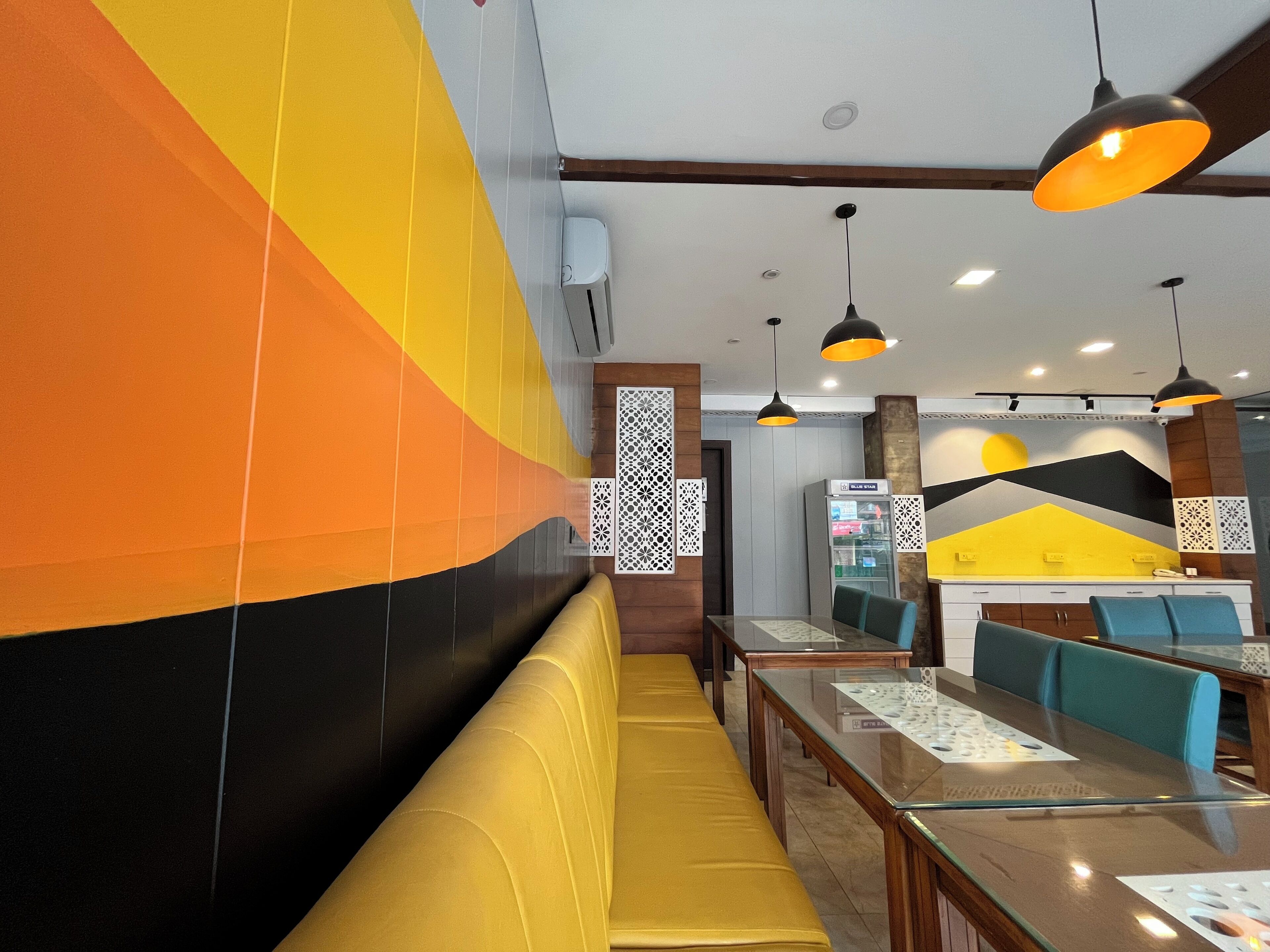 Interno di un ristorante con tavoli alti, sedute imbottite gialle e lampade a sospensione moderne.