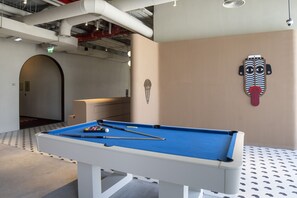 A pool table with billiard balls and cues, a wall-mounted decorative mask, and a hallway with an exit sign. - Executive Studio at Upside Living With Burj Views (Dubai)