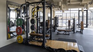 Une salle de sport équipée de matériel de musculation, de bancs et d’un miroir qui reflète l’espace.
