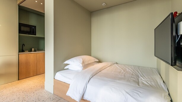Une chambre avec un lit, un téléviseur fixé au mur et un coin cuisine.