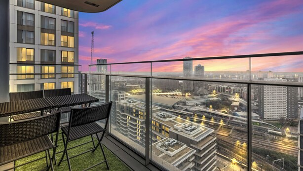 Un balcón moderno con vista a la ciudad al atardecer, con zona de comedor, sillas y mesa.