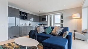 Una sala moderna con un sofá azul, una mesa de centro blanca y una cocina al fondo.