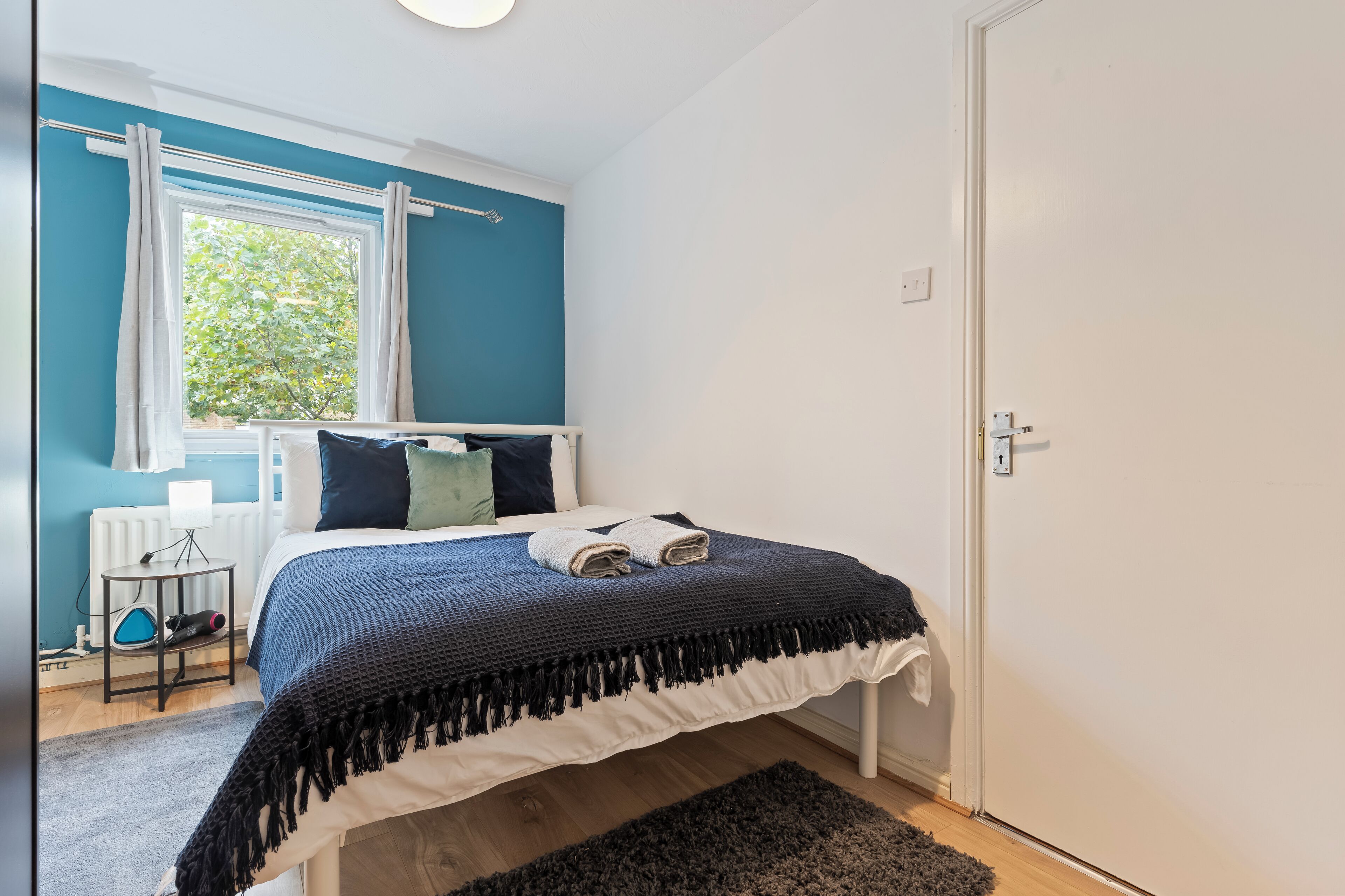 Ein Schlafzimmer mit Bett, Fenster mit Vorhängen, Heizkörper und Tür.