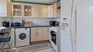A compact kitchen with a washing machine, a microwave, a stove, and cabinets. - Cozy London Townhouse With 4 Bedrooms (London)