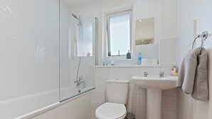 A modern bathroom with a glass shower enclosure, a white toilet, a sink, and a window. - Cozy London Townhouse With 4 Bedrooms (London)